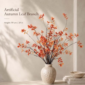 Puede incluir: Una rama artificial de hojas de otoño con follaje naranja y rojo sobre tallos finos y oscuros, con una altura de 99 cm. El texto Artificial Autumn Leaf Branch y Height: 99 cm / 39 in es visible en la esquina superior izquierda.