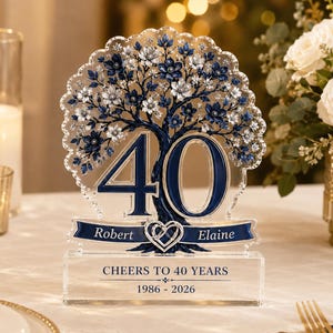 May include: A clear acrylic plaque featuring a tree with blue and silver flowers, the number 40, and a banner with the names Robert and Elaine. The base displays the text CHEERS TO 40 YEARS and 1986 - 2026, with a heart icon in the center.