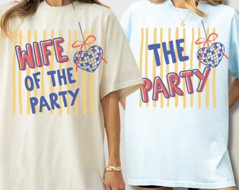 May include: Two short-sleeve t-shirts, one cream and one light blue, featuring vertical yellow stripes and a graphic of a heart-shaped disco ball with a red bow. The cream shirt reads WIFE OF THE PARTY and the blue shirt reads THE PARTY.