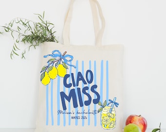 May include: A cream-colored canvas tote bag featuring a blue vertical striped pattern, a graphic of yellow lemons with a blue ribbon, and a blue mason jar illustration. The text reads CIAO MISS, Melissa's bachelorette, and NAPLES 2026.