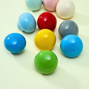 May include: A collection of ten round, smooth cabinet knobs in a variety of glossy colors including red, yellow, green, light blue, bright blue, grey, white, pink, and mint green, each featuring a polished finish and a spherical top shape.