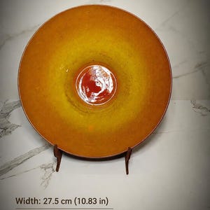 May include: A circular ceramic bowl featuring a gradient color scheme that transitions from a deep orange center to a bright yellow interior and a dark orange rim. The bowl measures 10.83 inches in width and 2.56 inches in height, displayed on a stand.