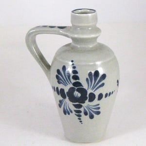 May include: A small gray ceramic pitcher with a blue floral design. The pitcher has a handle and a spout.