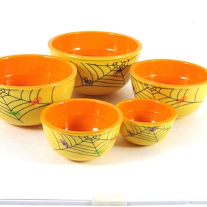 May include: Set of five yellow ceramic bowls with orange interiors and black spiderweb designs. The bowls are decorated with small colorful spiders.