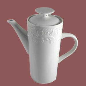 May include: A white ceramic coffee pot with a lid and handle. The pot has a tall, cylindrical body with a decorative floral pattern around the top. The spout is long and slender, and the handle is curved. The background is a solid maroon color.