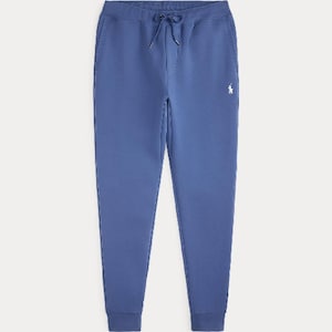Könnte beinhalten: Einfarbige blaue Jogginghose mit elastischem Bund und passendem Kordelzug, zwei Seitentaschen sowie gerippten Beinabschlüssen. Ein kleines weißes gesticktes Logo eines Pferdes mit Reiter befindet sich im Bereich des linken Oberschenkels.