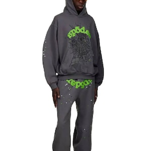 May include: A dark gray hoodie and matching pants set. The hoodie features a green spiderweb design and the word "sp5der" in green. The pants also have the word "sp5der" in green. Both pieces have white and silver paint splatter.