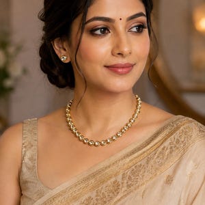 May include: A gold-toned necklace featuring a series of circular, bezel-set clear stones linked together in a continuous chain, accompanied by matching circular stud earrings with a single clear stone in each, worn with a beige sleeveless top.