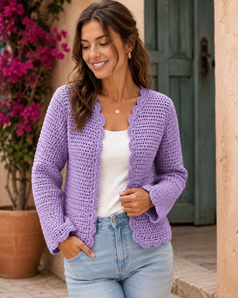 May include: A lavender crochet cardigan featuring long sleeves and a scalloped edge along the front opening and cuffs. The garment is worn over a plain white top and light blue denim jeans, showcasing a textured stitch pattern throughout the piece.