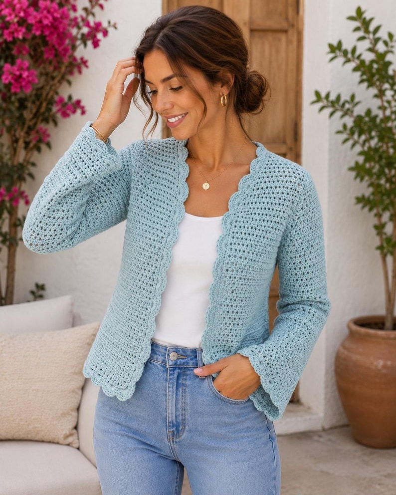 May include: A light blue crochet cardigan featuring long sleeves, a scalloped edge along the front opening, and a textured open-knit pattern. The garment is worn over a plain white top and light blue denim jeans, showcasing a consistent stitch design.