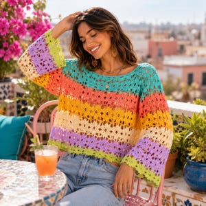 May include: A long-sleeved crochet jumper featuring horizontal stripes of lime green, lavender, cream, yellow, orange, and teal. The garment is constructed with a repeating floral pattern throughout, a wide round neckline, and loose, flowing sleeves.