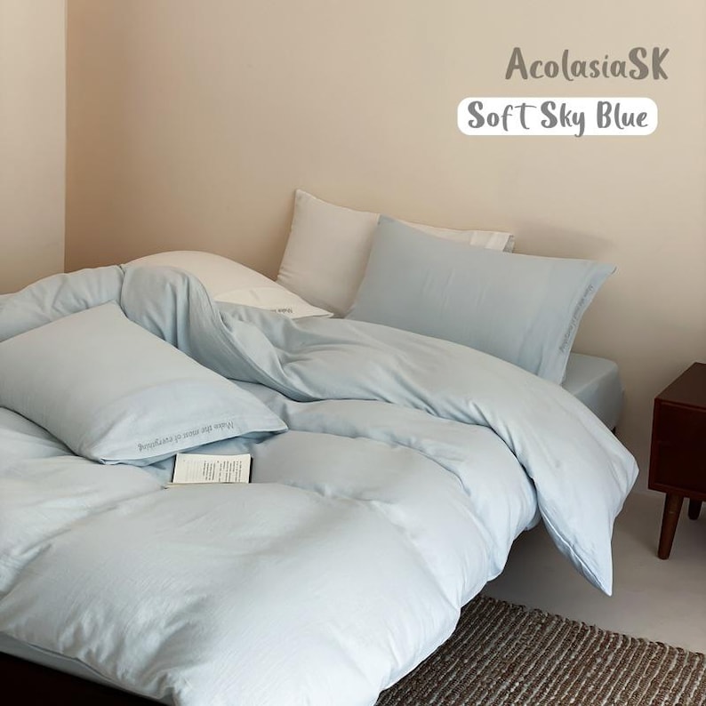 May include: A soft sky blue bedding set including a duvet cover and two matching pillowcases. The text AcolasiaSK and Soft Sky Blue is visible in the upper right corner. The bedding has a smooth, solid light blue color and a clean appearance.