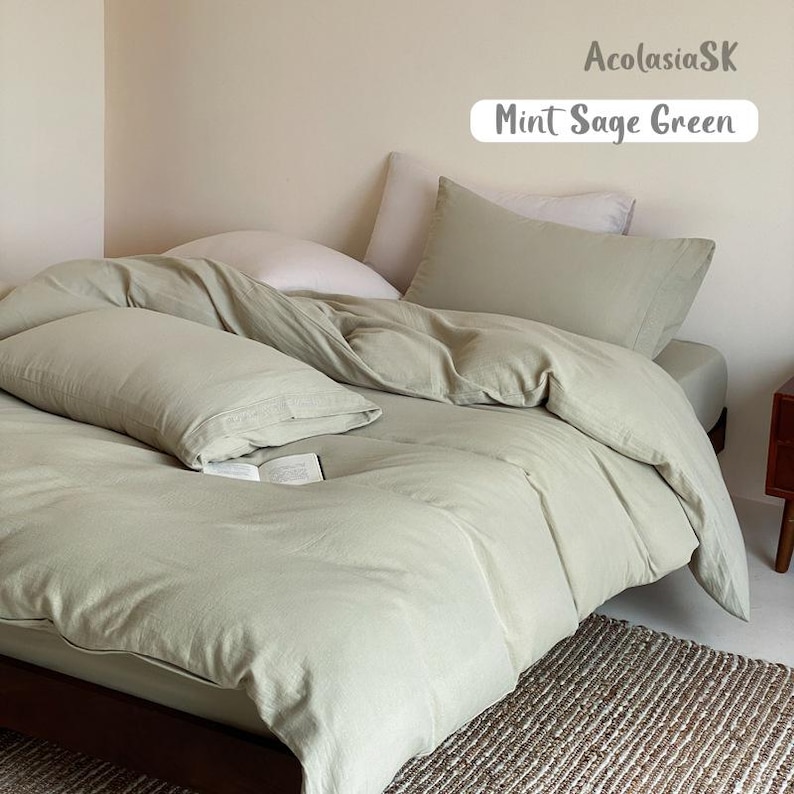 May include: A bed set featuring a mint sage green duvet cover and matching pillowcases. The text AcolasiaSK and Mint Sage Green is visible in the upper right corner. The bedding is arranged on a mattress with a light-colored pillow underneath.