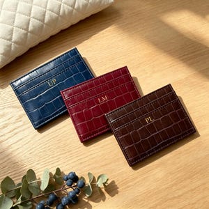 May include: Three rectangular card holders with a crocodile-embossed texture in navy blue, burgundy, and dark brown. Each holder features gold-colored embossed initials: UP on the blue, LM on the burgundy, and PL on the dark brown card holder.
