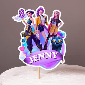 Könnte beinhalten: Ein weiß glasierter Kuchen mit einem individuellen Tortenstecker, der drei animierte Figuren, die Zahl 8 und ein violettes Banner mit dem in Weiß gedruckten Namen JENNY zeigt. Der Stecker enthält eine kleine blaue Kreatur und bunte Herzen.