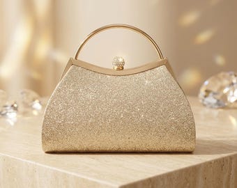 May include: A gold glitter clutch bag with a curved top edge, a thin circular gold metal handle, and a small spherical clasp adorned with clear crystals. The handbag features a textured, shimmering surface that reflects light across its exterior.