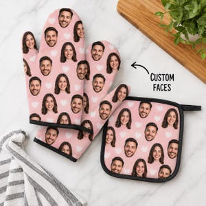 May include: A pink oven mitt and a square pot holder featuring a repeating pattern of various human faces and white heart icons. The text CUSTOM FACES is printed in black with an arrow pointing toward the kitchen textiles on a light surface.