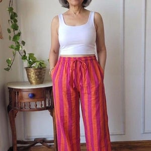 Peut inclure: Un débardeur blanc sans manches associé à un pantalon large à rayures verticales dans des tons vifs de rose fuchsia et d'orange. Le pantalon est doté d'une taille élastiquée avec un cordon de serrage assorti et deux poches latérales.