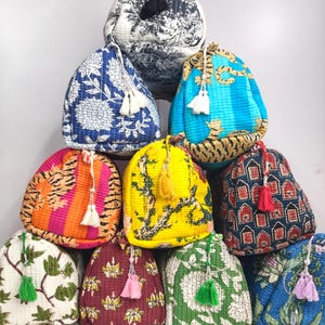 Peut inclure: Une collection de dix pochettes à cordon matelassées disposées en pyramide. Chaque pochette présente un motif de tissu unique, incluant des designs floraux, rayés tigre et géométriques, et est ornée d'un pompon décoratif sur le cordon.