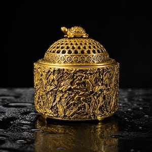 May include: A cylindrical gold-colored metal incense burner featuring intricate relief carvings of flying cranes across its body. The lid has a hexagonal lattice pattern and is topped with a small, sculpted turtle figurine in a matching gold finish.