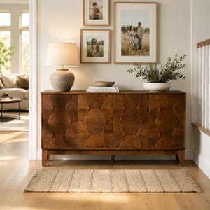 May include: A dark brown wooden sideboard featuring a geometric hexagonal pattern on its four cabinet doors. The sideboard is topped with a beige table lamp, a small wooden bowl, and two stacked books. A rectangular woven rug lies on the floor.