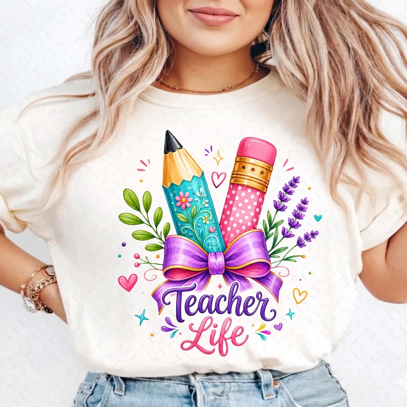 May include: A cream-colored t-shirt featuring a graphic print of a pencil and a pink eraser tied together with a purple bow. The design includes green leaves, purple lavender sprigs, small hearts, and the text Teacher Life in purple script.