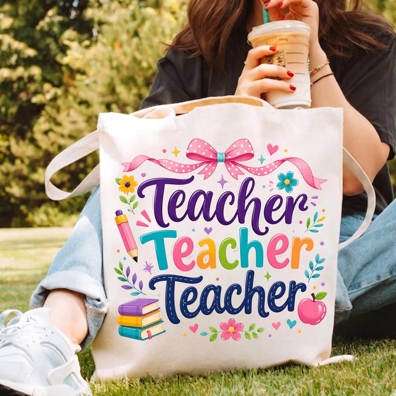 May include: A white canvas tote bag featuring a colorful graphic print with the repeated text "Teacher" in purple, teal, and orange. The design includes a pink polka-dot bow, a pink pencil, a stack of three books, a red apple, and small flowers.