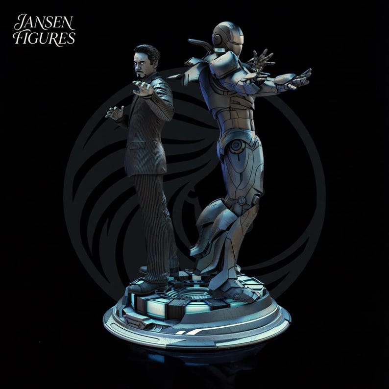 May include: A detailed statue featuring two figures: a man in a suit and an Iron Man suit. The figures are positioned back-to-back on a circular base. The statue is predominantly gray and black, with the text "Jansen Figures" in the upper left corner.