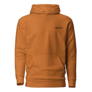 May include: A burnt orange hoodie with a front pocket and a drawstring hood. The upper right chest features the text "$50X" in black. The hoodie is made of a soft material.