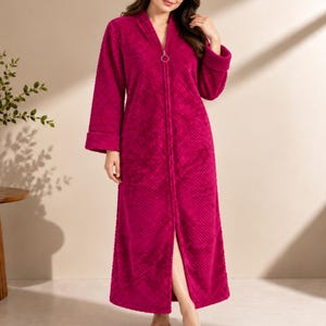 May include: A floor-length, magenta-colored robe featuring a textured, diamond-patterned fabric. This garment includes long sleeves with folded cuffs, a V-neckline, and a full-length front zipper closure finished with a circular metal ring pull.