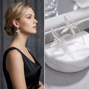 Può includere: Un paio di orecchini color argento caratterizzati da un delicato design floreale a più petali. Gli orecchini presentano un sottile perno a filo curvo che attraversa il lobo, creando una silhouette pendente di ispirazione botanica.