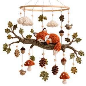 Peut inclure: Un mobile pour bébé en crochet composé d'une branche d'arbre marron centrale avec un renard orange et blanc endormi. Les éléments suspendus incluent des nuages crème, des feuilles de chêne vertes, des pommes de pin, des glands et des champignons.