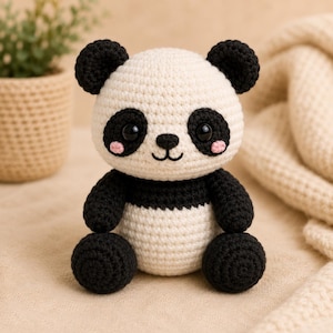 May include: A small, handcrafted crochet panda toy featuring a cream-colored head and body with black ears, arms, legs, and eye patches. The panda has large, glossy black eyes, a small black nose, a stitched mouth, and soft pink circular cheek accents.