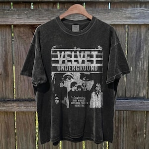 May include: A charcoal grey short-sleeve t-shirt with a distressed white graphic print featuring the text "the VELVET UNDERGROUND" and "featuring ANDY WARHOL'S EXPLODING PLASTIC INEVITABLE" above a black and white photographic collage of the band members.