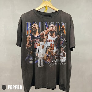 May include: Dark grey t-shirt with a collage of basketball player images and the name "BRUNSON". The player's jersey number "11" is visible. The shirt has a vintage, distressed appearance.