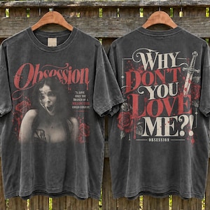 May include: A charcoal gray t-shirt featuring a graphic print on the front and back. The front displays a woman, the word "Obsession," and text reading "A love only the branch of a willow tree could conjure." The back features a sword, roses, and the text "Why don't you love me?!" with red accents.