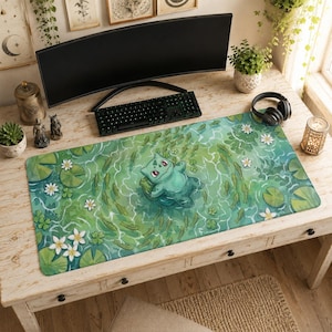 May include: A rectangular desk mat featuring a green Bulbasaur character floating in a pond filled with lily pads, white flowers, and small fish. The illustration uses shades of green and blue to depict water ripples and aquatic vegetation.