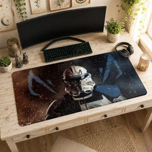 May include: A rectangular desk mat featuring a graphic illustration of a white and blue clone trooper helmet. The background transitions from a warm brown with orange sparks on the left to a dark blue with light blue streaks on the right side.