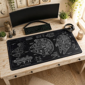 Pode incluir: Um tapete de secretária retangular grande e preto com uma ilustração técnica branca tipo planta do Millennium Falcon, incluindo vários esquemas rotulados, diagramas estruturais e detalhes mecânicos impressos na superfície.