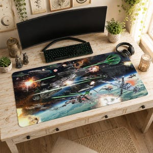 Puede incluir: Una alfombrilla de escritorio rectangular con una escena de batalla espacial con varias naves espaciales, explosiones y disparos láser. La alfombrilla tiene una combinación de colores azul y verde, con una representación detallada de un conflicto galáctico. Un teclado y un monitor están en el escritorio.