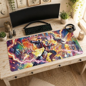 May include: A rectangular desk mat featuring a vibrant, multi-colored illustration of Transformers characters in a battle scene. The artwork displays Optimus Prime and other robotic figures amidst bright orange, yellow, and red lightning effects.