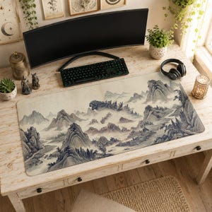 May include: A large rectangular desk mat featuring a detailed ink-wash style landscape illustration of misty mountains, pine trees, and a river. The artwork is rendered in shades of grey, beige, and muted blue, depicting a sprawling mountain range.