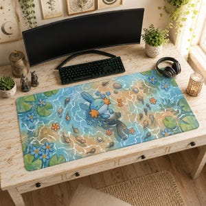 Puede incluir: Una alfombrilla de escritorio rectangular que muestra una superficie de agua azul claro con un personaje Mudkip flotando en el centro. El diseño incluye flores naranjas en forma de estrella, nenúfares verdes, peces grises y renacuajos.