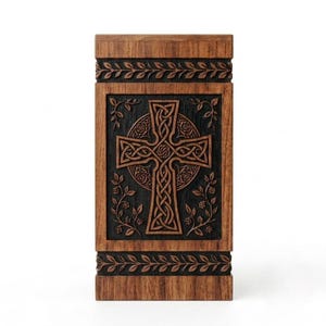 May include: A rectangular wooden urn featuring a dark brown finish with a central carved panel. The panel displays a detailed Celtic cross design surrounded by intricate floral vine carvings, framed by horizontal bands of leaf patterns at the top and bottom.