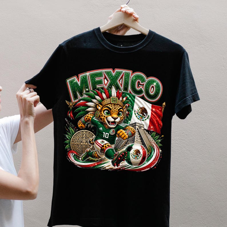 May include: A black t-shirt featuring a graphic print of a jaguar wearing a feathered headdress and a green soccer jersey with the number 10. The design includes the word MEXICO, a Mexican flag, a stone pyramid, and a soccer ball with the Mexican emblem.
