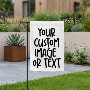 Op de afbeelding: Een witte rechthoekige tuinvlag die aan een zwarte metalen standaard hangt. De vlag bevat de zwarte tekst "YOUR CUSTOM IMAGE OR TEXT" gedrukt in een vet, schreefloos lettertype. Het ontwerp is gecentreerd op de stof die aan een haak hangt.