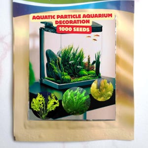 May include: A product package labeled AQUATIC PARTICLE AQUARIUM DECORATION 1000 SEEDS featuring a glass aquarium filled with green aquatic plants, dark rocks, and small fish, with three circular insets showing close-ups of different green plants.