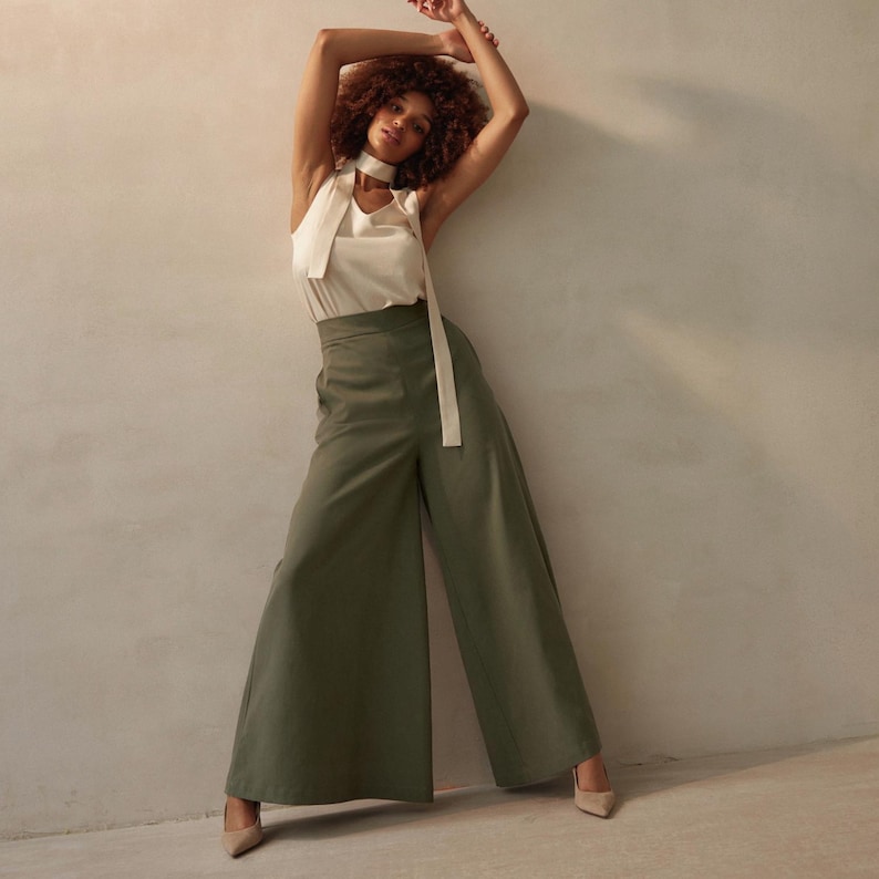 K&ouml;nnte beinhalten: Ein Damen-Outfit mit einem cremefarbenen Neckholder-Top mit langem, passendem Bindeband, kombiniert mit olivgr&uuml;nen Hosen mit weitem Bein. Das Outfit wird durch nudefarbene spitz zulaufende Abs&auml;tze erg&auml;nzt. Das Model hat lockiges braunes Haar.
