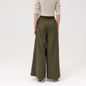 K&ouml;nnte beinhalten: Olivgr&uuml;ne Hose mit weitem Bein. Die Hose hat eine hohe Taille und eine flie&szlig;ende, lockere Passform. Das Model tr&auml;gt einen hellbeigen Pullover. Die Hose ist aus einem glatten, einfarbigen Stoff gefertigt.