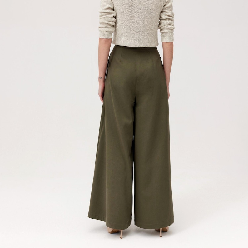 K&ouml;nnte beinhalten: Olivgr&uuml;ne Hose mit weitem Bein. Die Hose hat eine hohe Taille und eine flie&szlig;ende, lockere Passform. Das Model tr&auml;gt einen hellbeigen Pullover. Die Hose ist aus einem glatten, einfarbigen Stoff gefertigt.